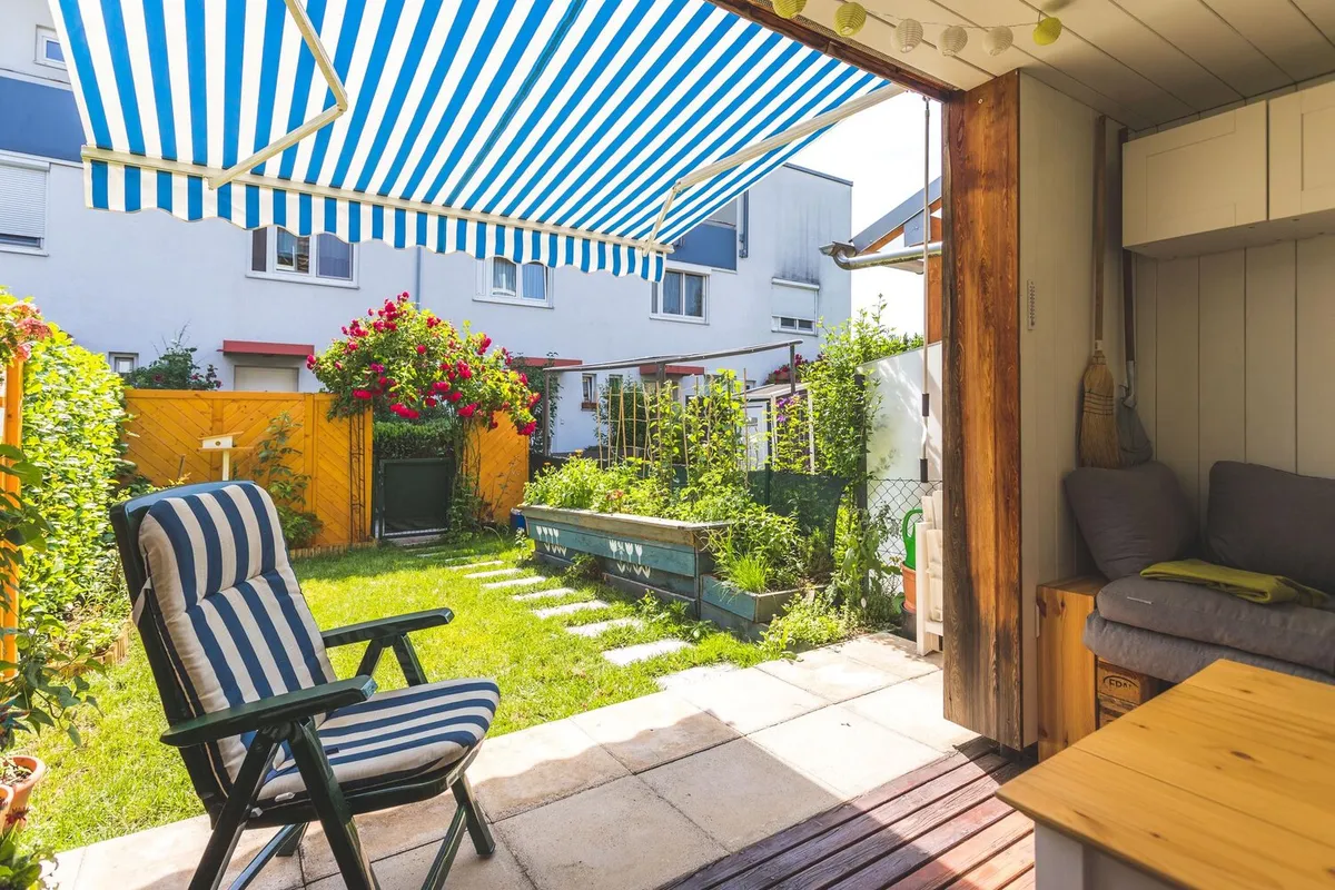 Store banne à toile rayée bleue et blanche déployé au-dessus de la terrasse dallée d'une maison avec jardin